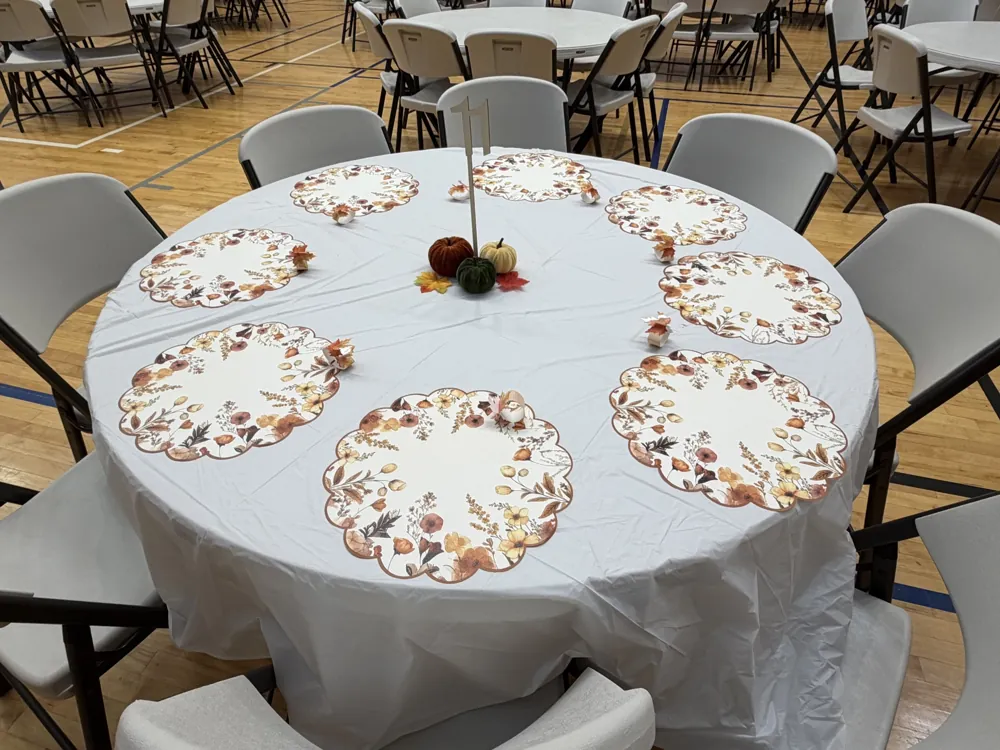 Round table decorated with autumn floral placemats and a small pumpkin centerpiece
