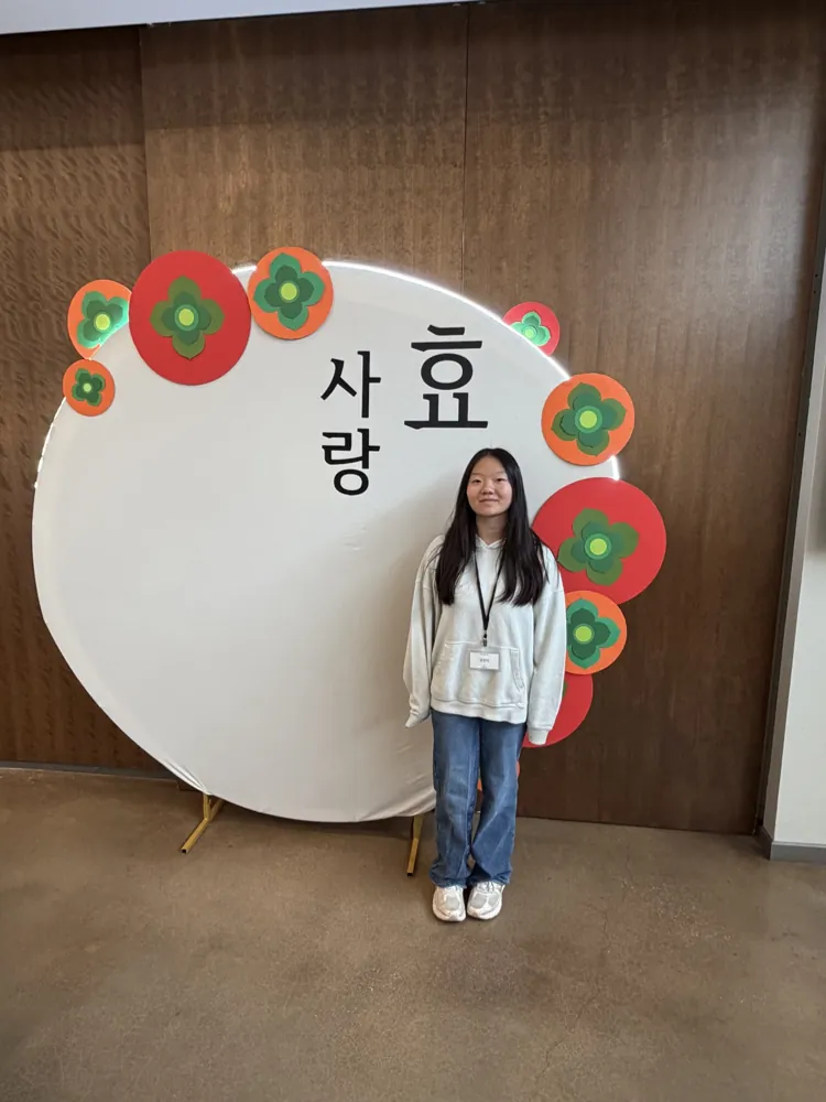 Generational Club member volunteering at the event, standing in front of a backdrop reading 효 사랑 (filial love)