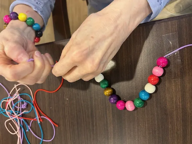 A resident and volunteer stringing a beaded bracelet together