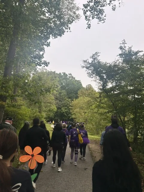 Walkers in purple shirts heading down a tree-lined path during the Walk to End Alzheimer's