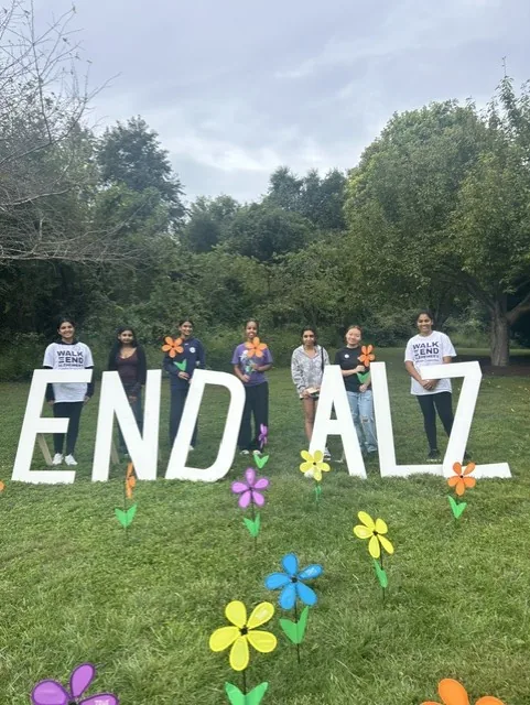 Club members standing among the "END ALZ" letters with pinwheel flowers